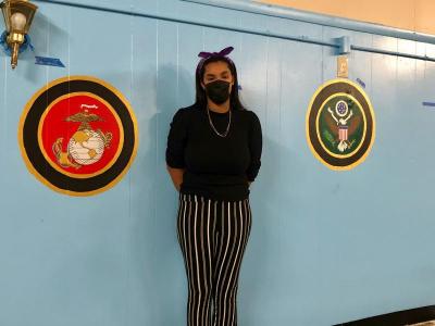 Gomes poses with her in-progress mural, which features the emblems of each branch of the armed services. Photo by: Madison Czopek