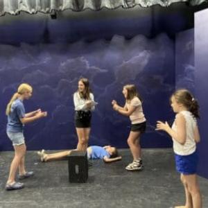 Five young women act out a scene on stage in a class